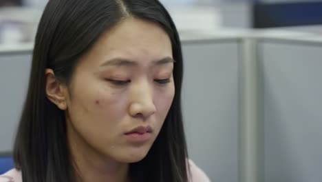 a young professional sits attentively at her desk in an office setting, deeply focused on her work. the environment is busy, reflecting a typical day at the office.