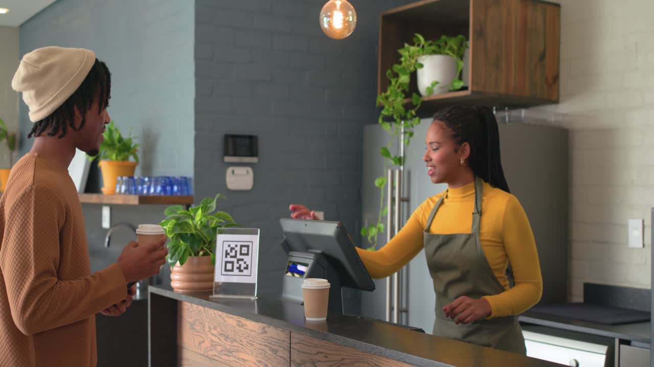 Homem afro-americano usando o celular no balcão de um café após receber um prompt de QR code, barista entregando um copo, espaço para texto