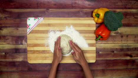 A-Top-view-of-making-flour-dough-on-cutting-board-on-the-wooden-table,-two-big-yellow-and-red-capsicums-and-a-green-broccoli-on-the-table