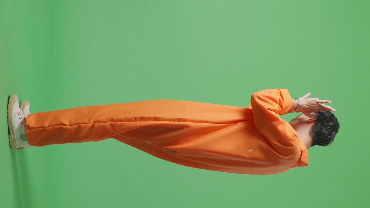 손잡이에 인 아시아 남성 수감자의 전체 몸의 측면 뷰는 녹색 화면 배경에 서서 손바닥 표시를 보여주며 카메라에 의해 포착되기를 원하지 않는 표정을 나타니다.