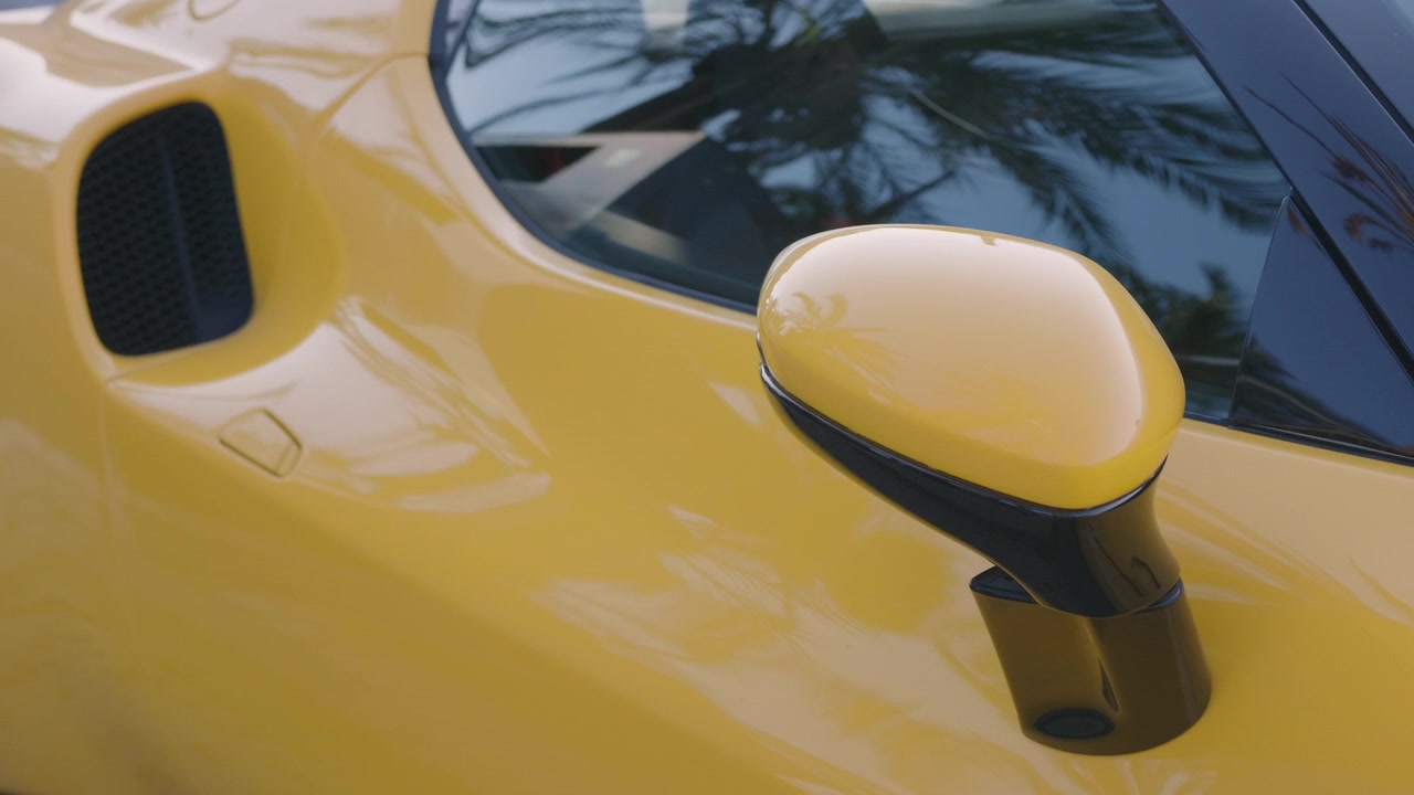 Primo piano dello specchietto laterale e della presa d'aria di un'auto sportiva gialla con riflessi di palme, Costa Azzurra, Francia.