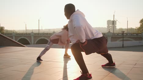 couple wearing sportswear stretching on the street at sunset