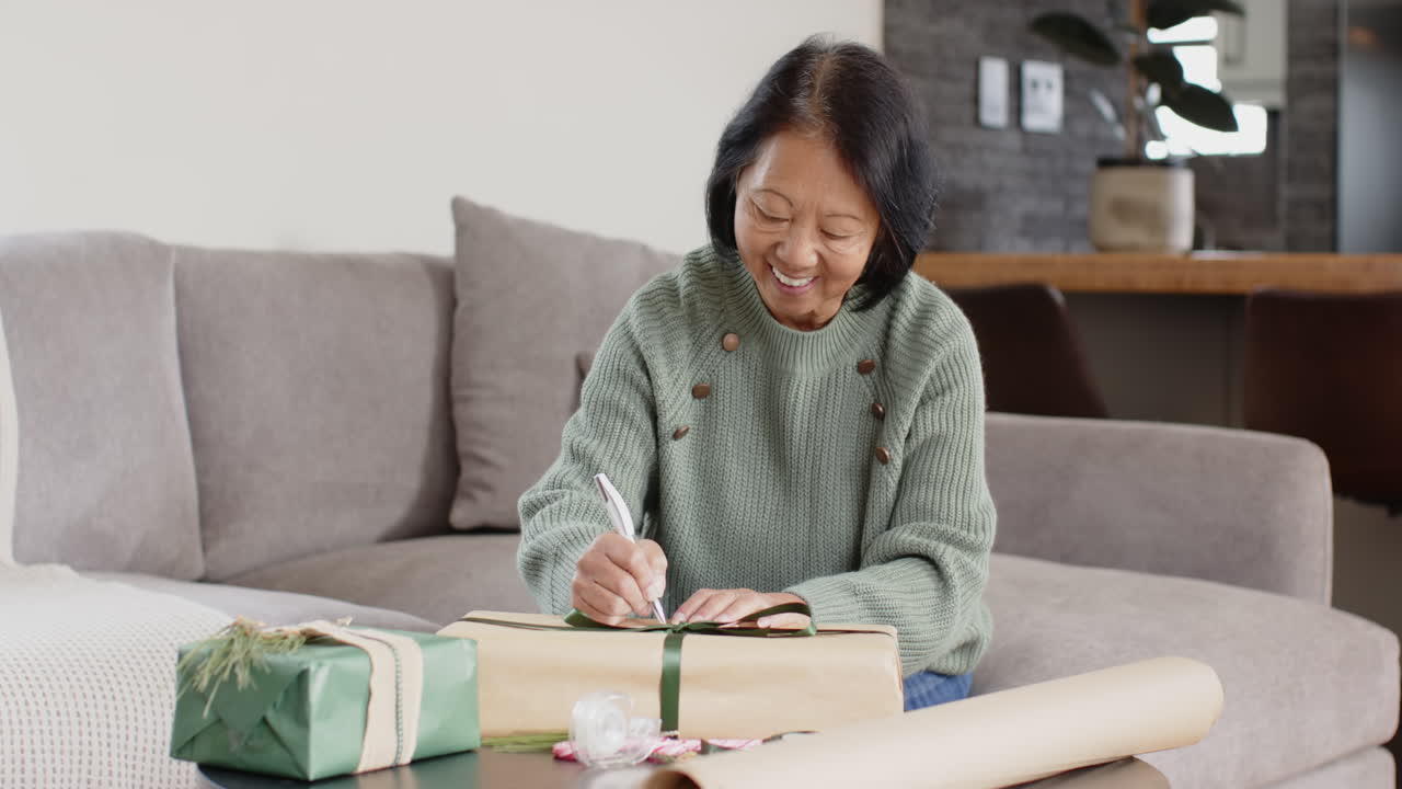 Smiling senior woman wrapping Christmas gifts at home, enjoying holiday preparations