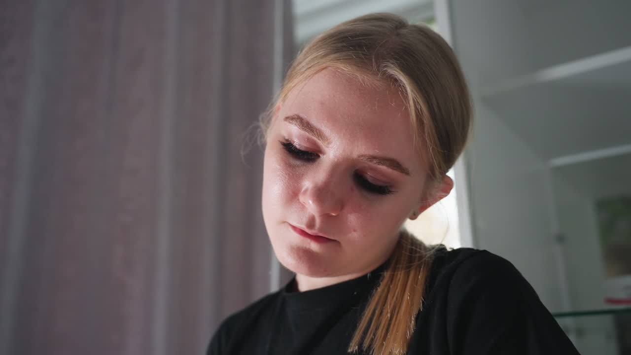 Close up of blonde female massage therapist deeply focused on task with soft natural light reflecting on her face, blurred cabinet and curtain background adding serene ambiance to indoor setting