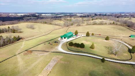 aerial reveal of a large green horse barn in the middle of the bluegrass state frankfort kentucky with grand blue sky vistas and gorgeous evergreen trees and dynamic shadows