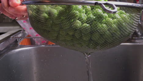 footage of woman washing and rinsing green peas with inox colander in a sink slow motion