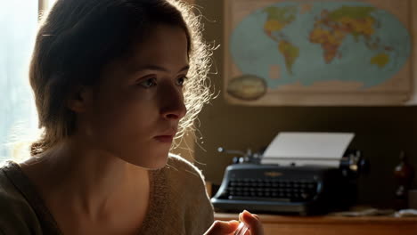 young woman deep in thought with pen, typewriter, and world map