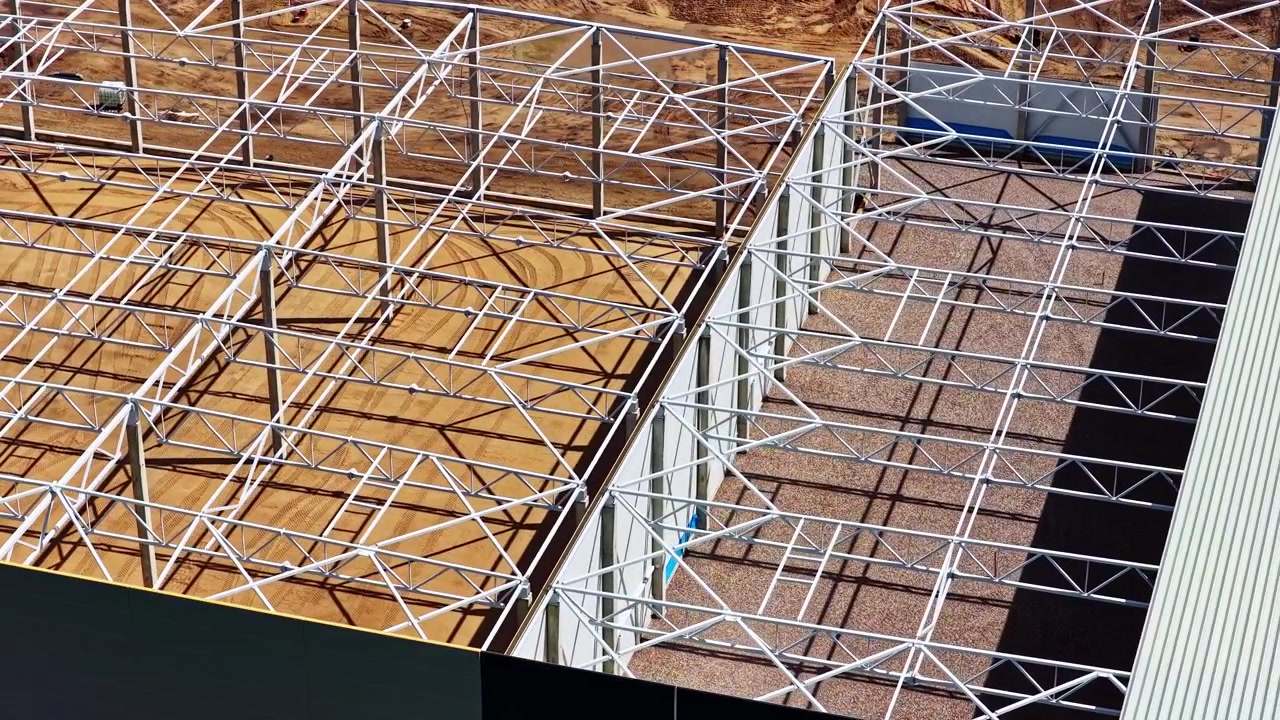 New industrial building's steel roof structure and metal framework under construction in aerial view