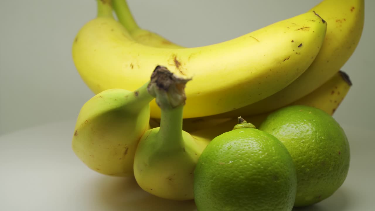 노란색 익은 바나나와 라임이 색 배경으로 테이블에 회전 - 근접 촬영