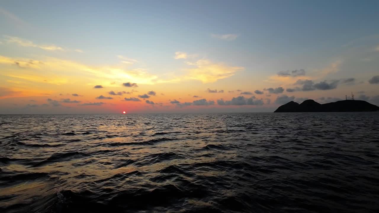 An orange sunset with clouds in the blue sky, captured from a boat over the Caribbean Sea.