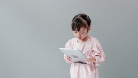 Child-watching-a-cartoon-with-a-digital-tablet-in-the-studio-with-a-gray-background-and-copy-space