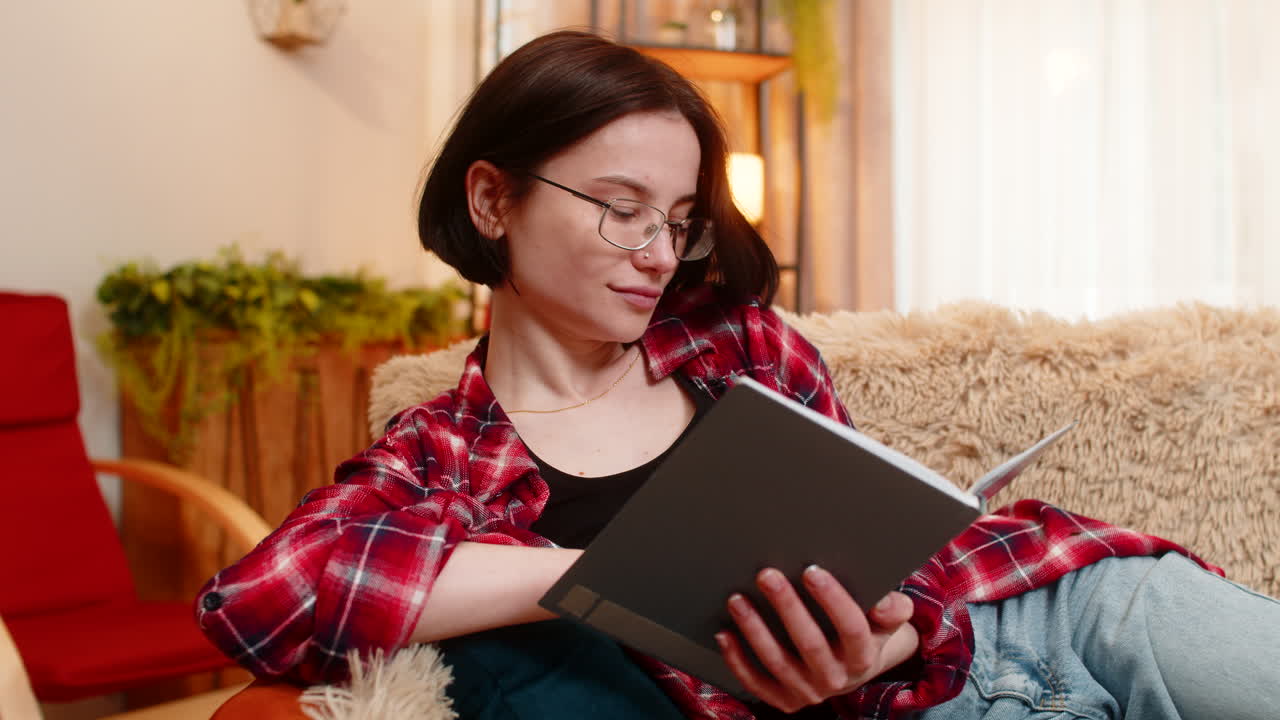 Young woman reading old journal notebook at home smiling thoughtfully with soft nostalgic emotion