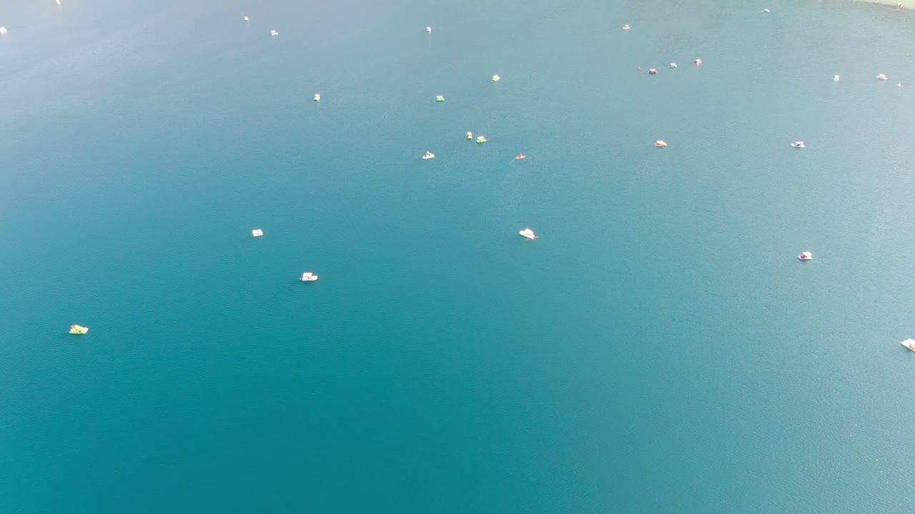 Drone view in Greece top view over a light and dark blue lake with small boats and surrounded by green mountain on a sunny day in Crete