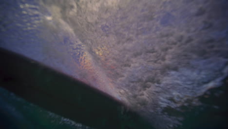 surfer rides on pink board across wave, view from underwater