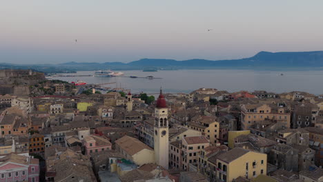 panoramic drone shot over the old town of corfu during dawn, flying above saint spyridon church with swallows in the morning sky