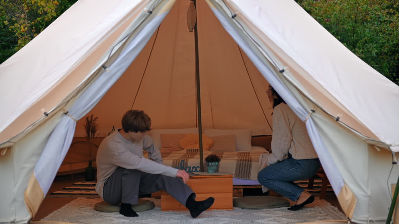 Et par, der snakker og går ind i et telt ved glamping. Frodig skov omkring