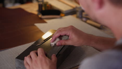 Man-covers-sandpaper-with-chalk-at-table-in-workshop