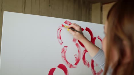 close-up of unrecognizable female artist paints red peonies or other flowers with brush on the canvas. the artist paints pink flowers on canvas with thick brush, close-up