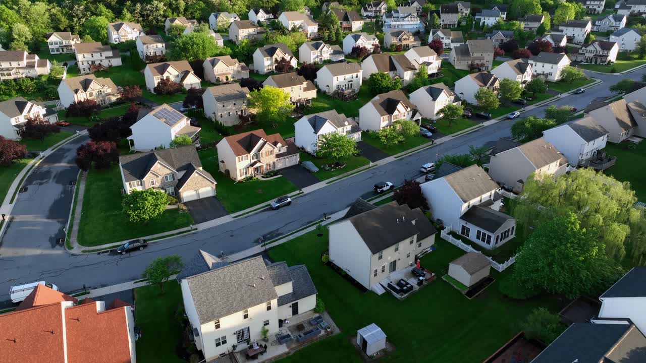 Two-story american one family houses with garden and double garage in quiet american neighborhood. Sunset time with green trees in spring. Suburb district located on hilltop on the evening. Aerial.