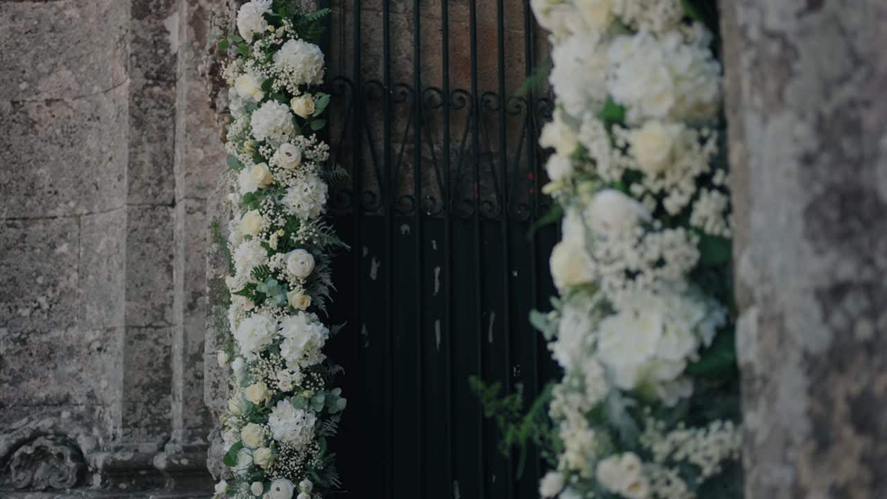 Fiori bianchi rigogliosi fiancheggiano un antico portale per un ingresso nuziale senza tempo.