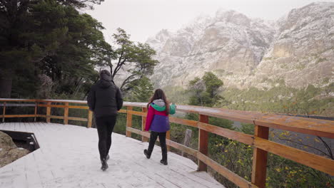 mother and daughter enjoy peaceful walk along snowy wooden path surrounded by forest and mountains in bariloche, argentina