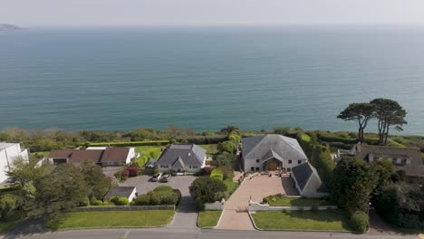 aerial view of private cliffside community with luxury homes, manicured gardens and tall hedges overlooking a calm ocean horizon, exemplifying exclusive coastal living