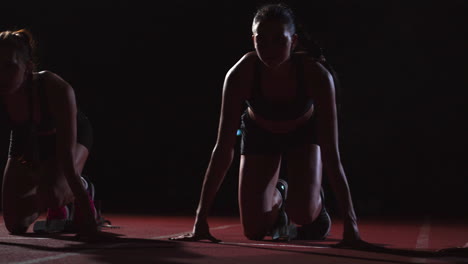 female runners at athletics track crouching at the starting blocks before a race. in slow motion.