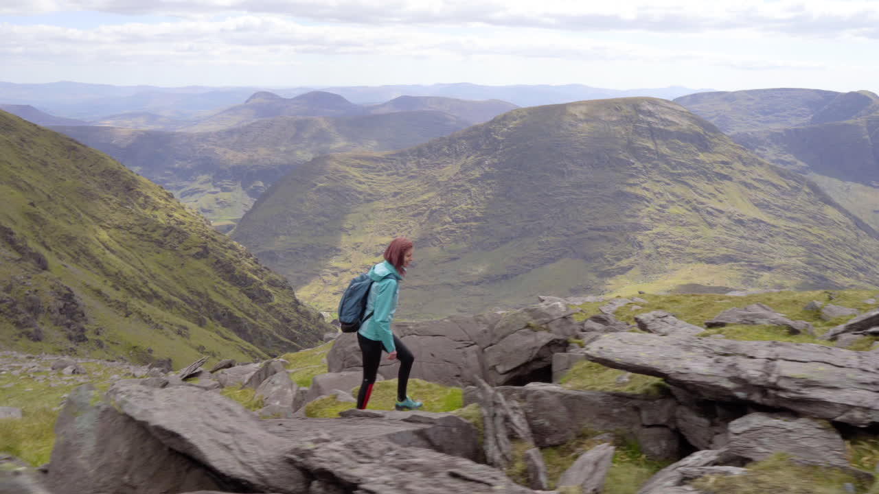 disparo lateral de seguimiento de una chica feliz caminando y caminando en el sendero de alta montaña al aire libre en la naturaleza en irlanda en mcgillycuddy reeks en 4k