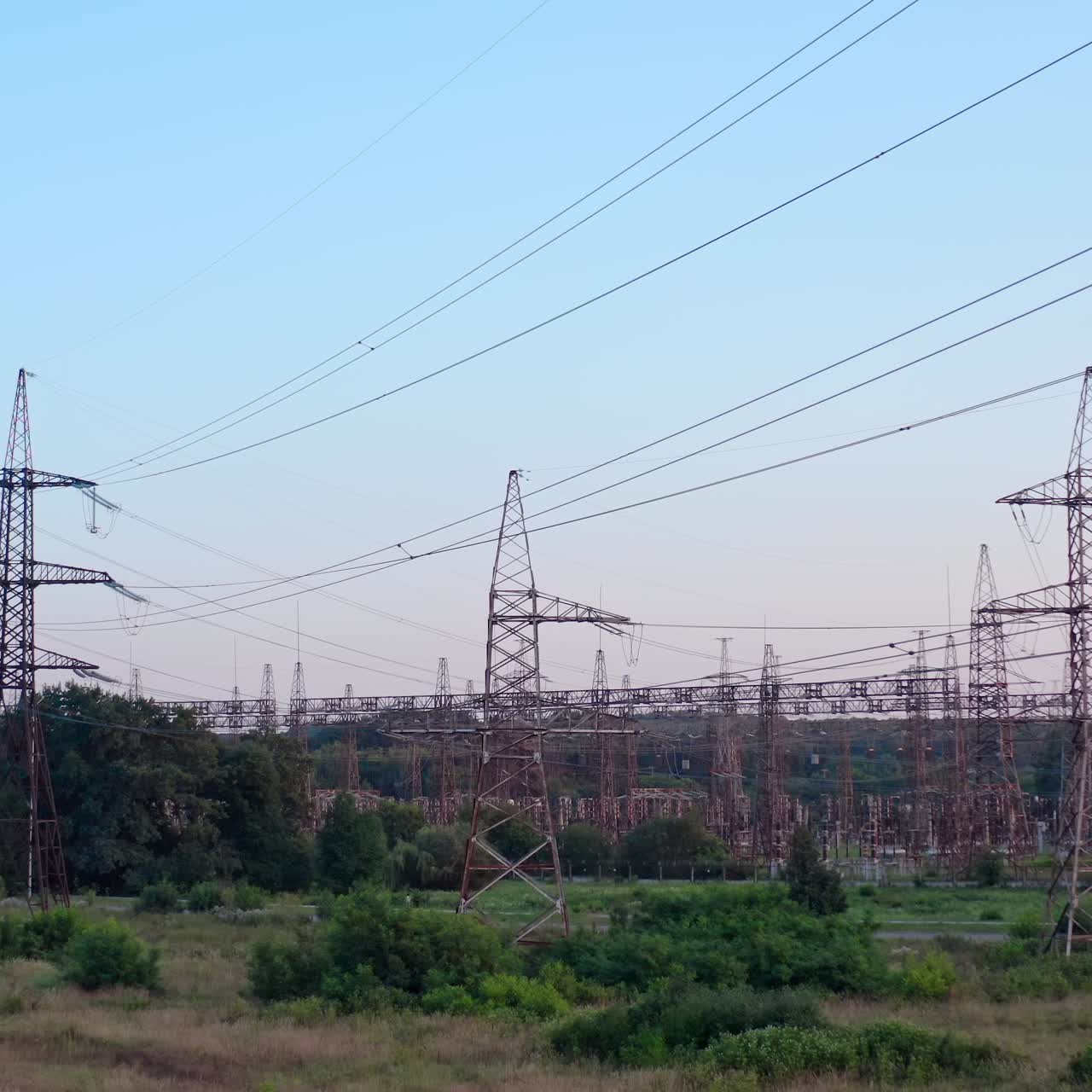 Lots of electricity towers on field. Large power station with many high-voltage electric lines with wires against the sky background. Transmission lines in green nature
