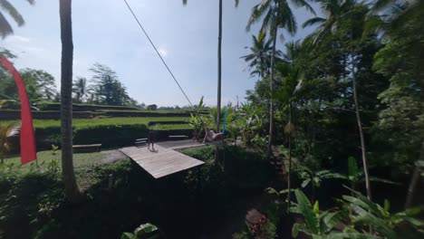 slowmotion fpv rotating shot of a beautiful lady swinging on a swing set in the tropical nature in a large dress