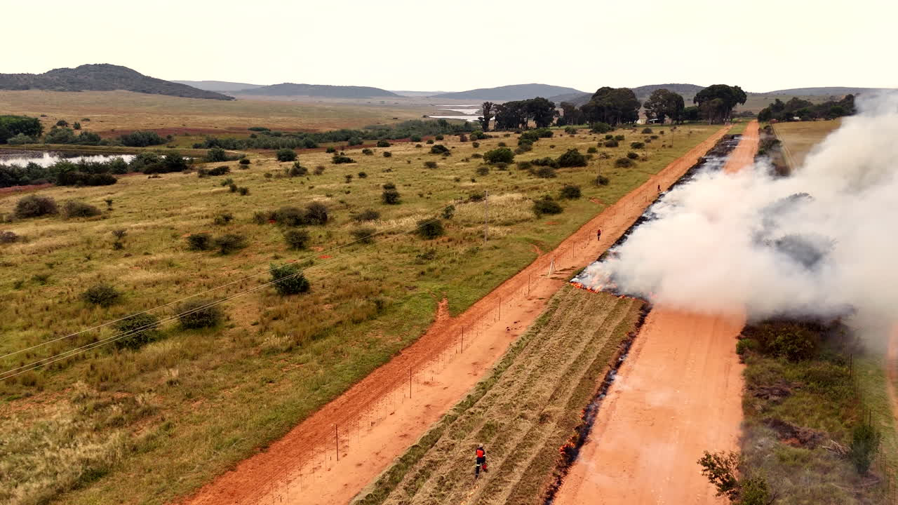 Smoke rise from fire trail being burned by laborers in rural countryside, aerial
