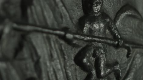 close up of a medival metal plate found in innsbruck, austria, displaying a person with a spear. racking focus with shallow depth of field. shot in 4k. with a slight panning movement. moody lighting.