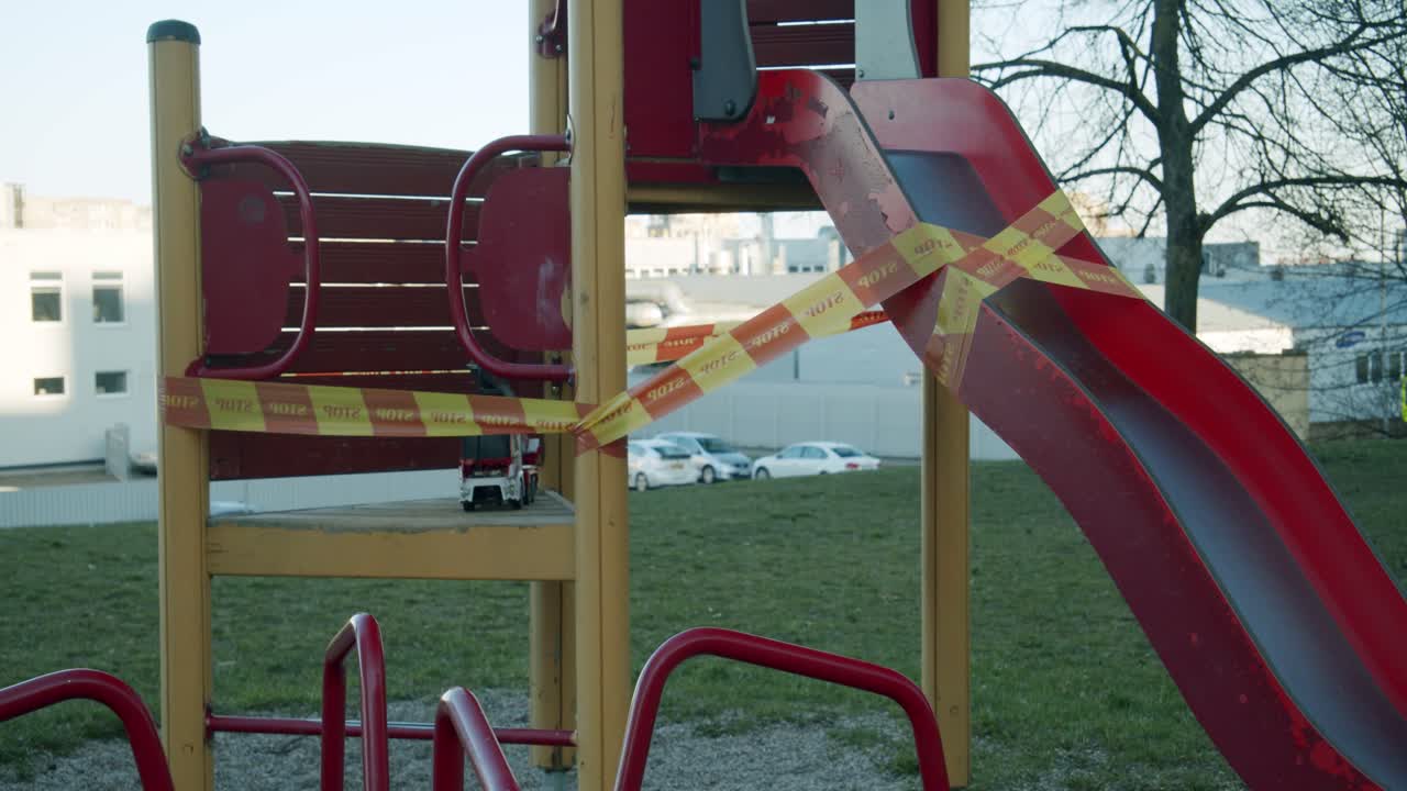 A Closed Down Slide and a Toy in an Empty Kids' Playground Wrapped in Yellow and Red "STOP" Caution Tape due to Quarantine