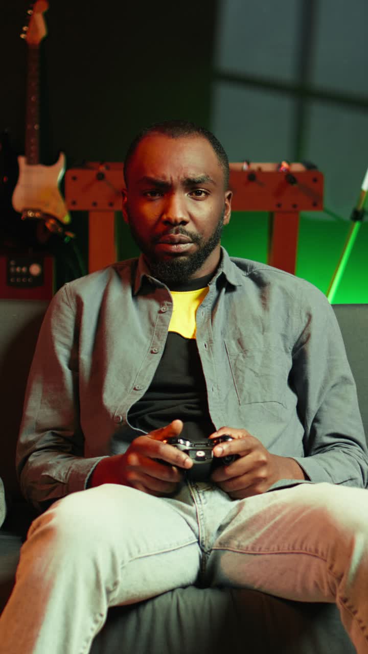 Vertical video Focused gamer in RGB lit home gaming with gamepad, enjoying himself
