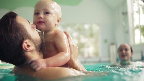 Cute-baby-having-swimming-lesson-with-his-mother-and-father.-Healthy-family-teaching-their-baby-to-swim-in-the-swimming-pool