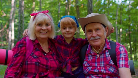 Old-senior-grandparents-couple-tourists-hikers-resting-in-forest-with-granddaughter-in-summer-wood