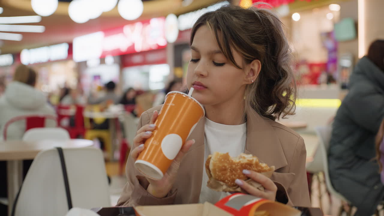 Un influencer disfruta de comida rápida, de un ambiente relajado de fin de semana con una reseña espontánea de comida y bebida, reacción natural de un influencer saboreando un refresco y una hamburguesa en medio de la vibrante iluminación de un centro comercial