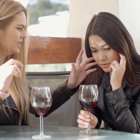 blond woman comforting friend over glass of wine