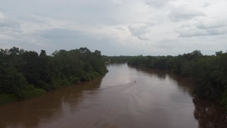 cinematic aerial view of a boat crossing the river in the middle of the rainforest