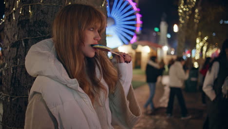 woman biting colorful lollipop in luna park reading smartphone message closeup.