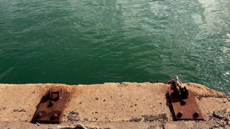 rusty iron fixtures on a dock in heraklion crete greece with green water shimmering below
