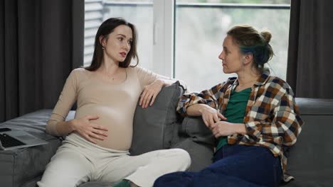 woman touching pregnant belly, talking about pregnancy with friend