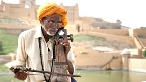 an old traditional man playing sarangi (an string instrument) against the historic fort.