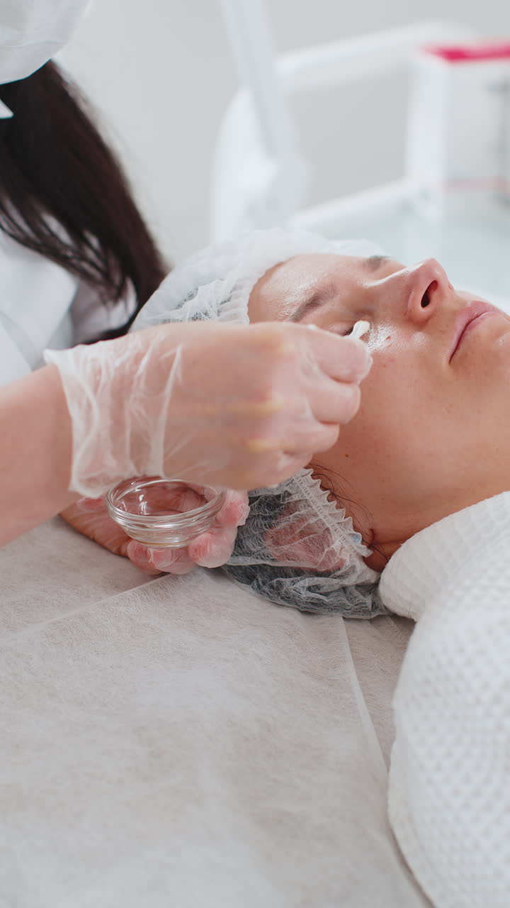 Cosmetologa che applica un peeling acido idratante sulla pelle intorno agli occhi di una donna per un trattamento anti-età.