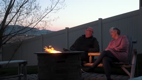 loving, senior, retired couple sitting warm at a fire pit at dusk