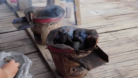 close-up of a person refilling charcoal in a traditional thai clay charcoal stove with embers smoking for barbecue cooking. the scene captures the essence of rural thai cooking methods