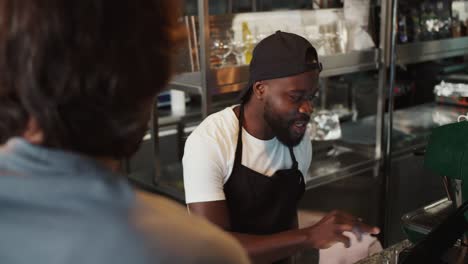 Doner-worker.-A-Black-person-in-a-black-cap-takes-an-order-on-an-electronic-guy-against-the-background-of-a-doner-market.-Service-in-a-fast-food-restaurant