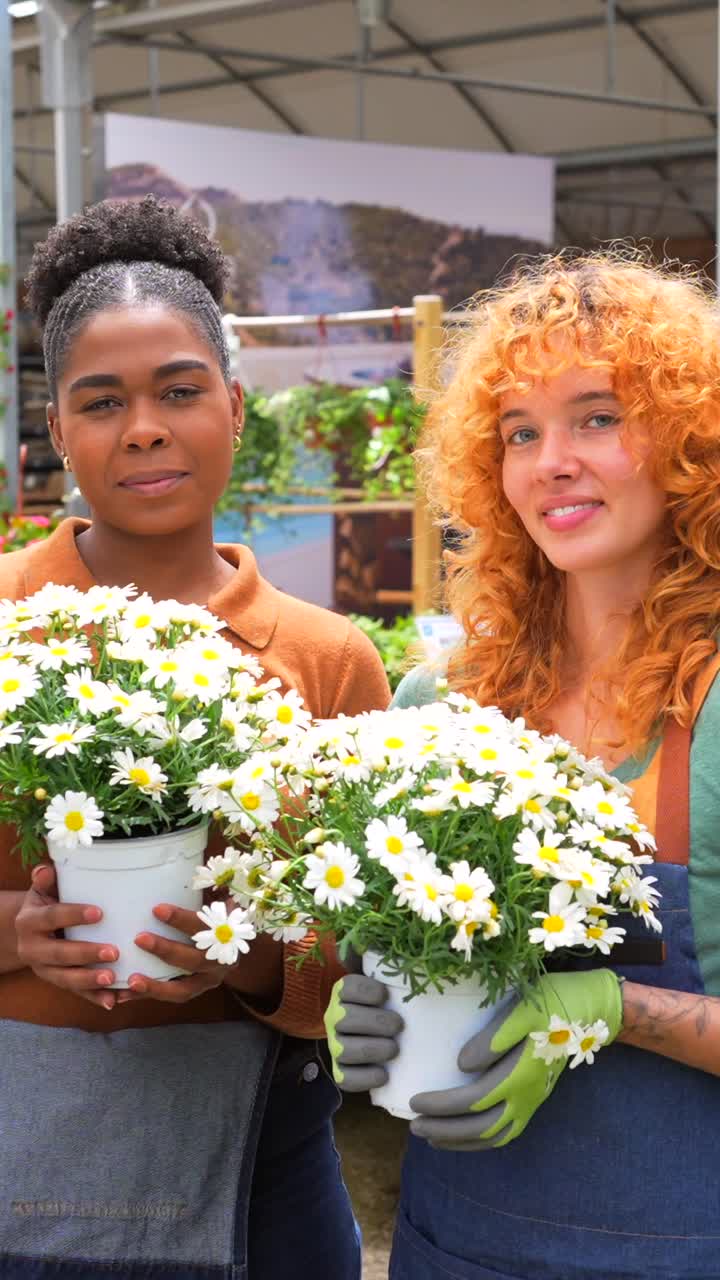Two women holding pots of daisies