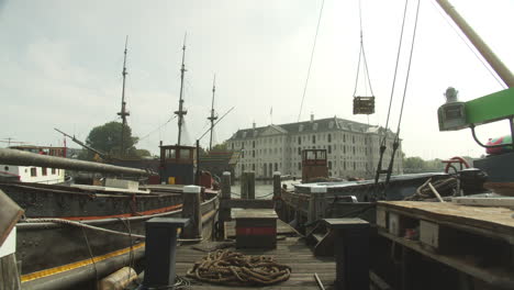 Details-Of-A-Wooden-Jetty-In-Amsterdam,-Netherlands-With-A-View-Of-The-National-Maritime-Museum-And-Amsterdam-Ship-Replica-In-The-Background---tilt-down-shot