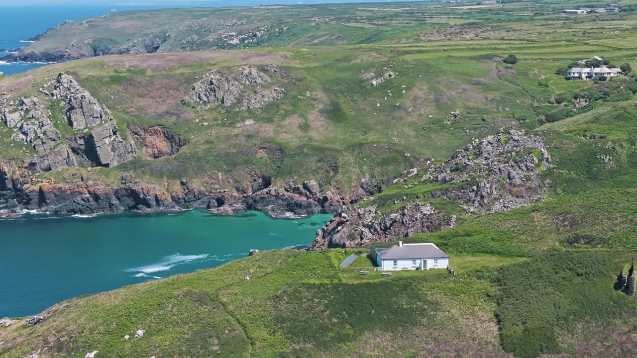 Aerial circle left view over Cornwall coast showing lush cliffs, blue ocean, and open sky, small home above